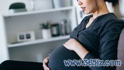 Relaxed young Asian pregnant woman gently touching her belly while sitting on bed at home. Mother-to-be. Expecting a new life. Love and bonding. Pregnancy health and wellness concept